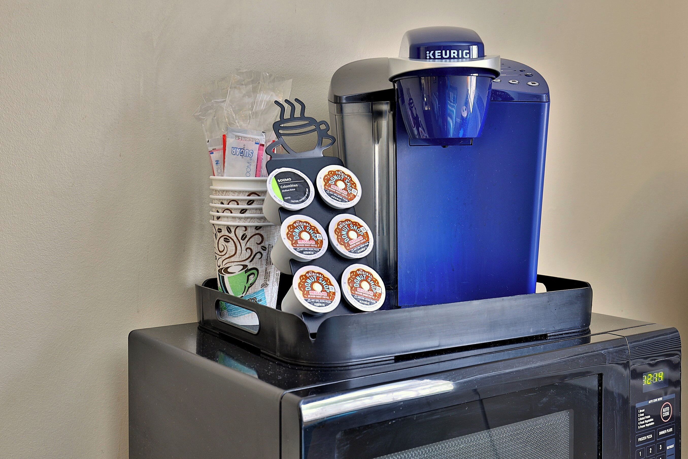 En kaffemaskine med en blå vanddispenser og en holder til kaffekapsler med flere kapsler.