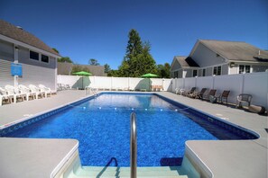 A rectangular swimming pool with a metal ladder leading into it, surrounded by lounge chairs and umbrellas.