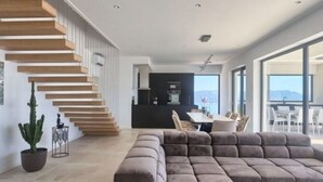 A modern living room with a large sectional sofa, a staircase with wooden steps, and a dining area with a table and chairs. - Villa Ateneum Comfortable Holiday Residence (Labin)