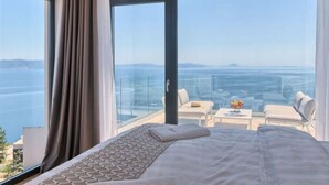A hotel room with a large bed, a view of the sea, and a balcony with seating. - Villa Ateneum Comfortable Holiday Residence (Labin)