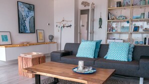 Un salon moderne avec un canapé gris, des coussins à motifs bleus, une table basse en bois et une bibliothèque remplie de divers objets.