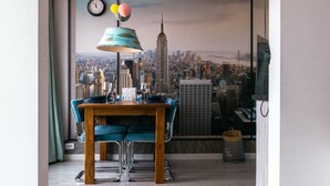 Un coin repas avec vue sur la ville, une table avec des chaises, une lampe suspendue et une horloge au mur.