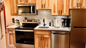 Une cuisine moderne dotée de meubles en bois, d’appareils électroménagers en acier inoxydable, notamment un four à micro-ondes, un four et un réfrigérateur, ainsi que d’un évier.