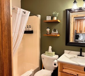 A bathroom with a shower curtain, a toilet with a tissue box, and wooden shelves with decorative items. - Newly Remodeled Fireplace Studio Ski-in/Ski-Out Condo-Balcony, Pool & Hot Tub (Lutsen)