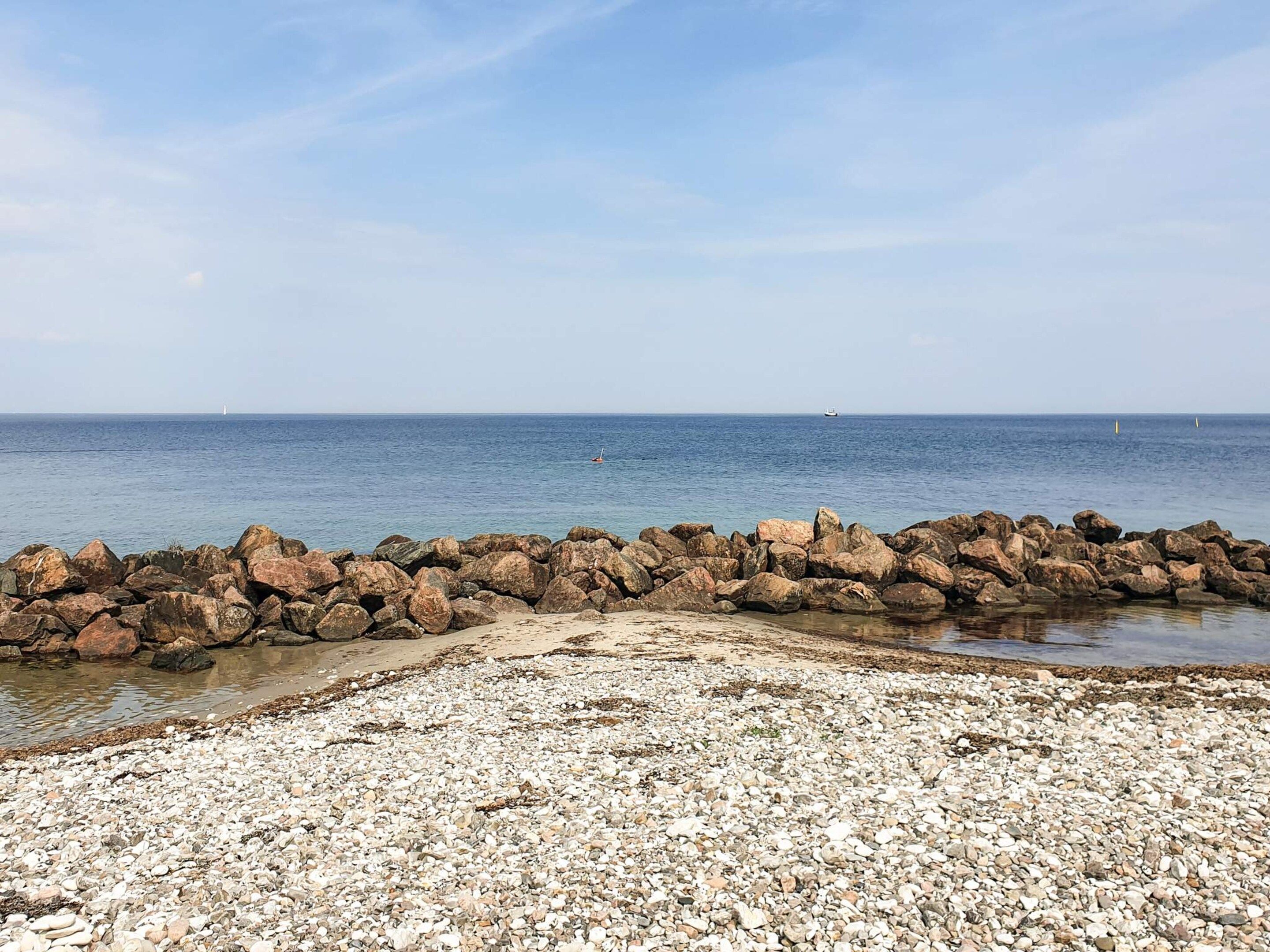 A rocky shoreline with a clear view of the sea and distant boats.