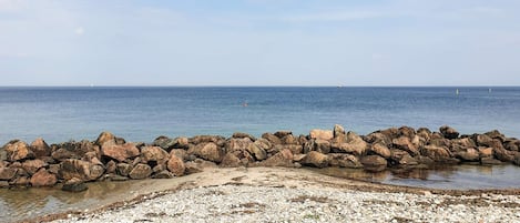 A rocky shoreline with a clear view of the sea and distant boats.
