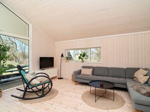 A modern living room with a sofa, a television, a rocking chair, and a large window. - 5 Star Holiday Home in Hundested (Hundested)