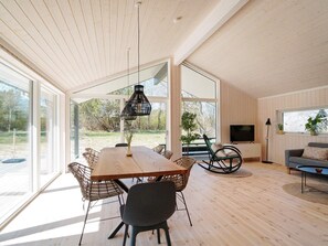A spacious living area with a wooden dining table, modern chairs, a black hanging light fixture, a television, and a sofa.