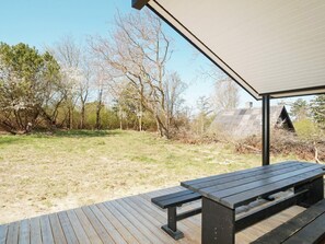 An outdoor wooden deck with a picnic table, surrounded by trees and a grassy area. - 5 Star Holiday Home in Hundested (Hundested)