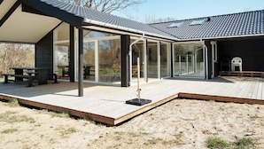A modern outdoor patio with glass walls, a wooden deck, and a covered seating area. - 5 Star Holiday Home in Hundested (Hundested)