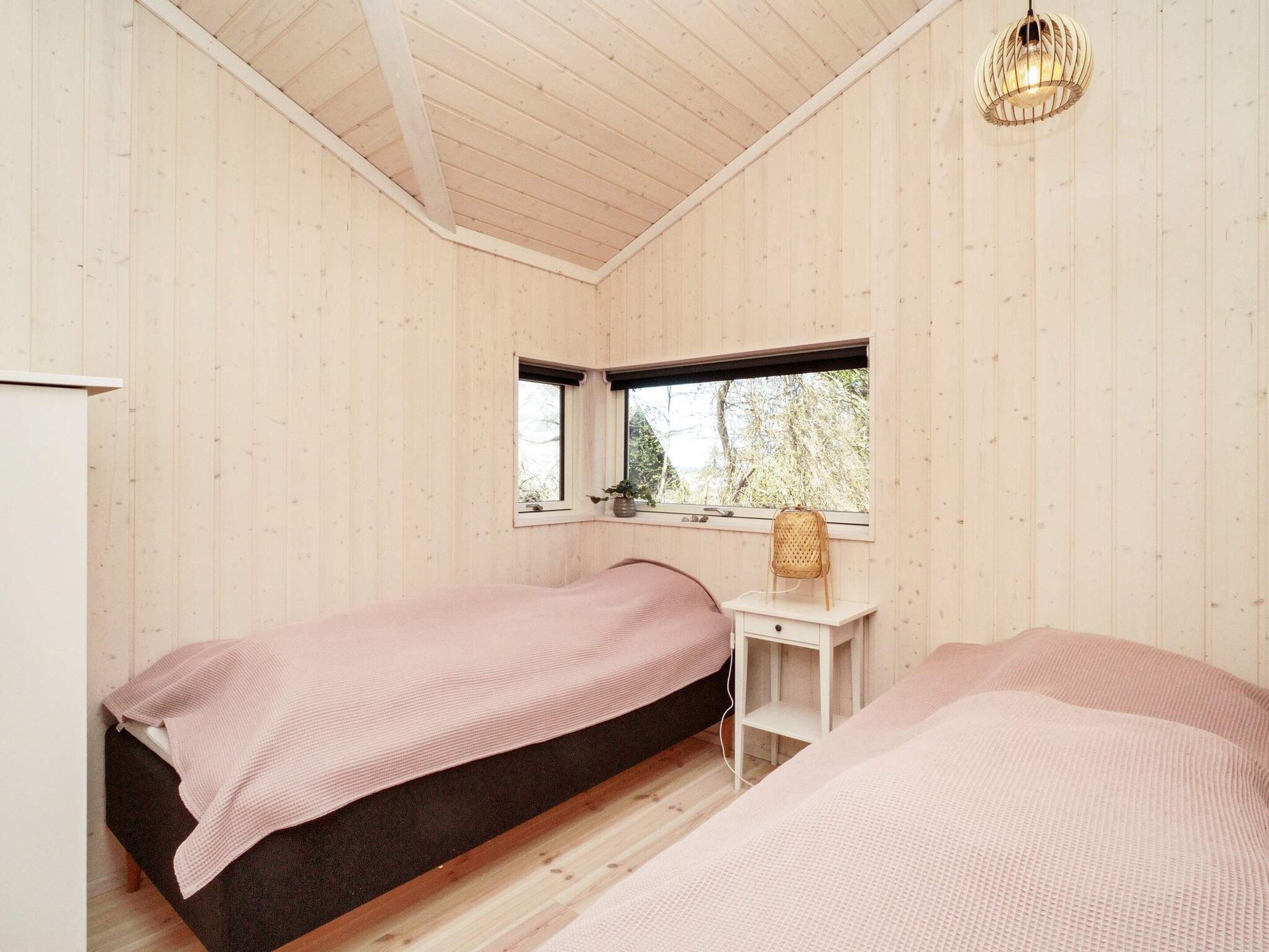 A room with two beds, a small desk, a window, and a hanging light fixture.