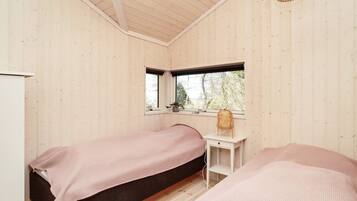 A room with two beds, a small desk, a window, and a hanging light fixture.