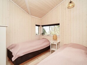 A room with two beds, a small desk, a window, and a hanging light fixture.