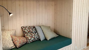A cozy room with a wooden slatted wall, a green cushioned bench, and a single floor lamp.