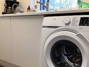 A front-loading washing machine with a control panel, a coffee maker, and a bottle of soap on the countertop.