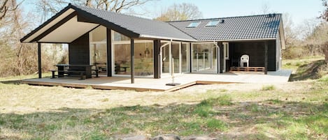 A modern house with a covered patio, a fire pit, and a large windowed area.
