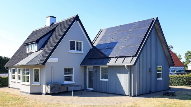Een twee verdiepingen tellend huis met een schuin dak, zonnepanelen en een klein terras.