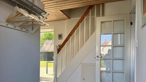 Een gang met een houten trap, een witte deur met glaspanelen en een metalen kapstok.