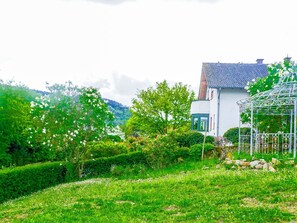 Stroll through the serene garden, surrounded by lush greenery and vibrant flowers, with a picturesque view of the hilly landscape.