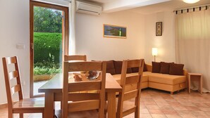 A living room with a wooden dining table, chairs, a sofa, and a small side table. There is a picture on the wall and a window with a view of greenery outside. - Apartment in Croatia Near the Coast (Medulin)