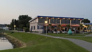 Um edifício moderno com área de estar coberta ao ar livre, um pequeno espelho d'água e um gramado bem cuidado.
