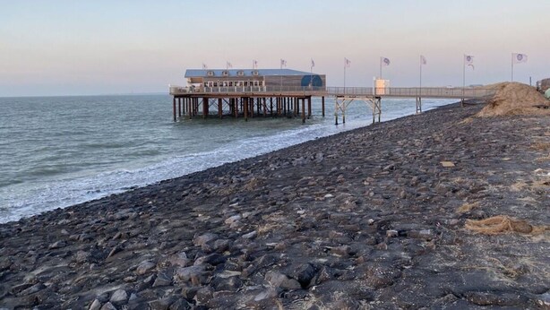 Um cais que se estende para o mar, com um edifício na extremidade.