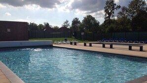 Uma piscina retangular com água cristalina, rodeada por um deck ladrilhado e uma fileira de cadeiras reclináveis azuis.