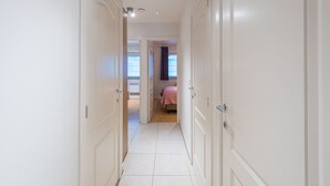 Un pasillo estrecho con puertas blancas que dan a un dormitorio con cama y ventana.