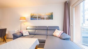 Una sala de estar moderna con un sofá gris, una mesita, una lámpara y un ventanal grande.