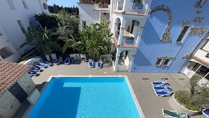 Une piscine entourée de chaises longues, elle-même bordée d’immeubles dotés de balcons et de plantes.