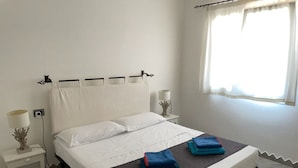 Un lit bien fait, avec du linge de lit blanc, une tête de lit sombre et deux serviettes pliées posées sur le pied de lit.