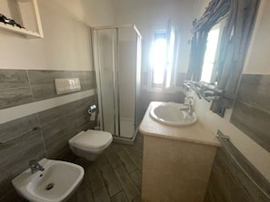 Une salle de bain comprenant des toilettes, un bidet, un lavabo et une douche à parois de verre.