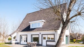 Une maison à deux étages avec un toit en tuiles, un petit balcon et un jardin devant la maison, avec une table et des chaises.