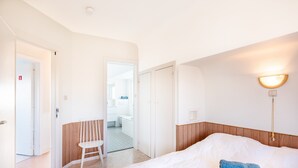 Une chambre d’hôtel avec un grand lit, une lampe de chevet, une tête de lit en bois et un petit tabouret.