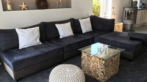 A modern living room with a dark sectional sofa, a glass coffee table, and a decorative wall piece above the sofa. - Holiday Apartment Summer Breeze (Bad Zwischenahn)