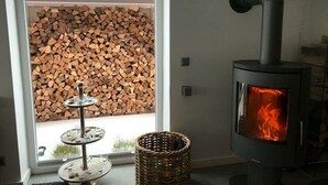 A modern room with a wood-burning stove, a three-tiered metal stand, and a wicker basket. - Holiday Apartment Summer Breeze (Bad Zwischenahn)