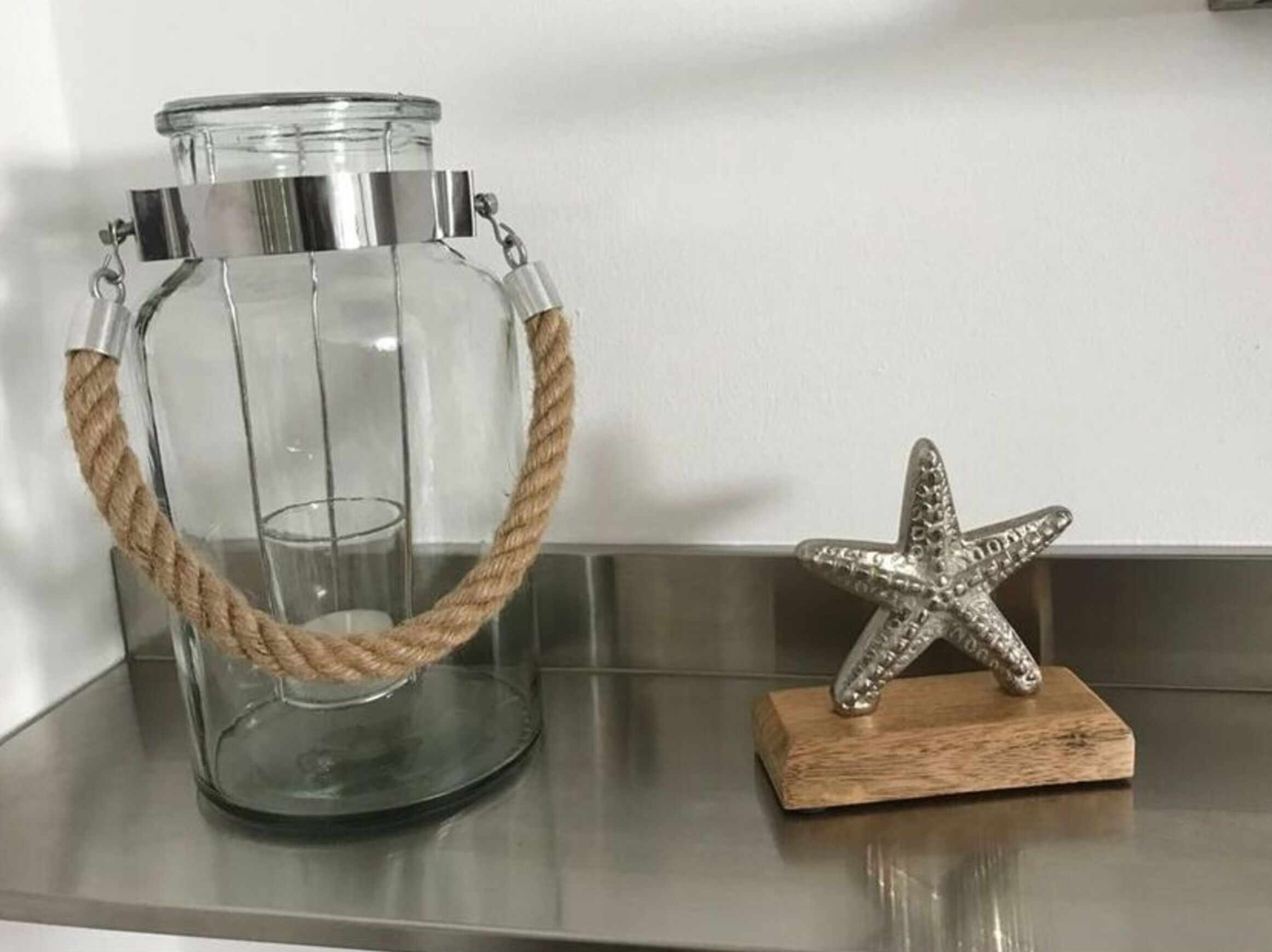 Um frasco de vidro transparente com alça de corda e um enfeite de estrela-do-mar sobre uma base de madeira.