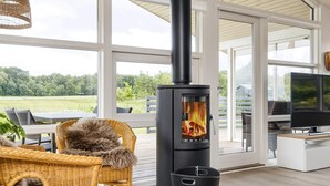 A modern living room with a large black wood-burning stove, wicker furniture, and a glass table.
