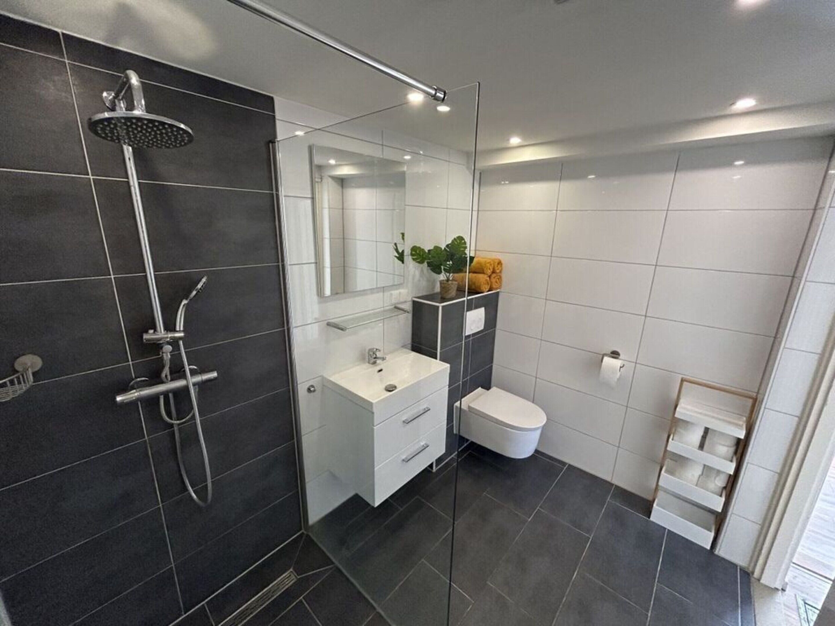 Ein modernes Badezimmer mit Duschkabine, weißem Waschtisch, Toilette und Handtuchhalter.