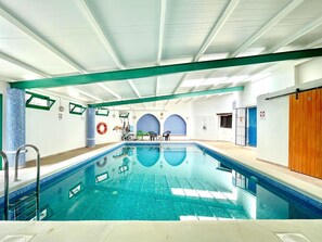 Ein großer, überdachter Swimmingpool mit klarem, blauem Wasser, umgeben von gefliestem Boden und Wänden.
