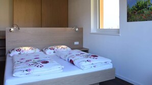 A bedroom with a wooden headboard, a window with a view of greenery, and a bed with floral bedding. - Magdalena at the Urbanhof (Bolzano)