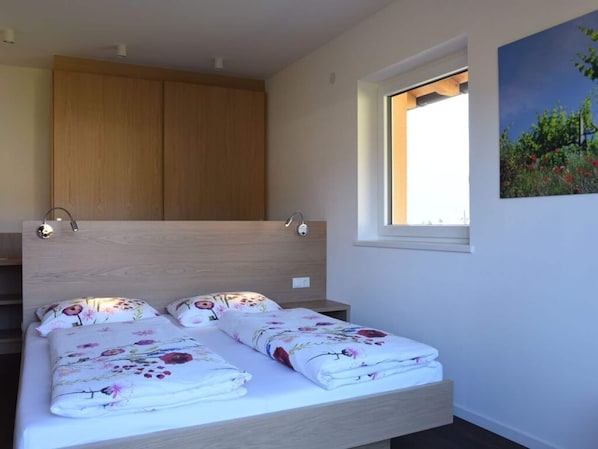 A bedroom with a wooden headboard, a window with a view of greenery, and a bed with floral bedding. - Magdalena at the Urbanhof (Bolzano)