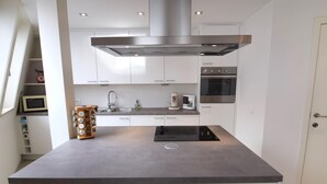 A modern kitchen with white cabinets, a stainless steel range hood, a built-in oven, and a coffee maker. - Apartment in a Central Location (Blankenberge)