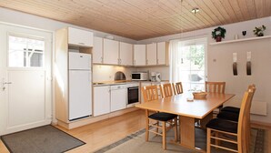 A modern kitchen with white cabinets, a wooden dining table, and a black rug. - 6 Person Holiday Park Home in Grasten (Grasten)