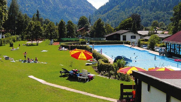 A pool area with a view of mountains, surrounded by a lawn with lounge chairs and umbrellas.