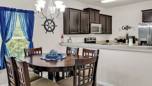 Una cocina moderna con armarios de madera oscura, una isla central con sillas, una lámpara de araña y un timón de barco colgado en la pared.