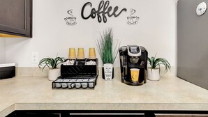 Una encimera de cocina con una estación de café, que incluye una cafetera, tazas y un adorno de pared con motivos de café.