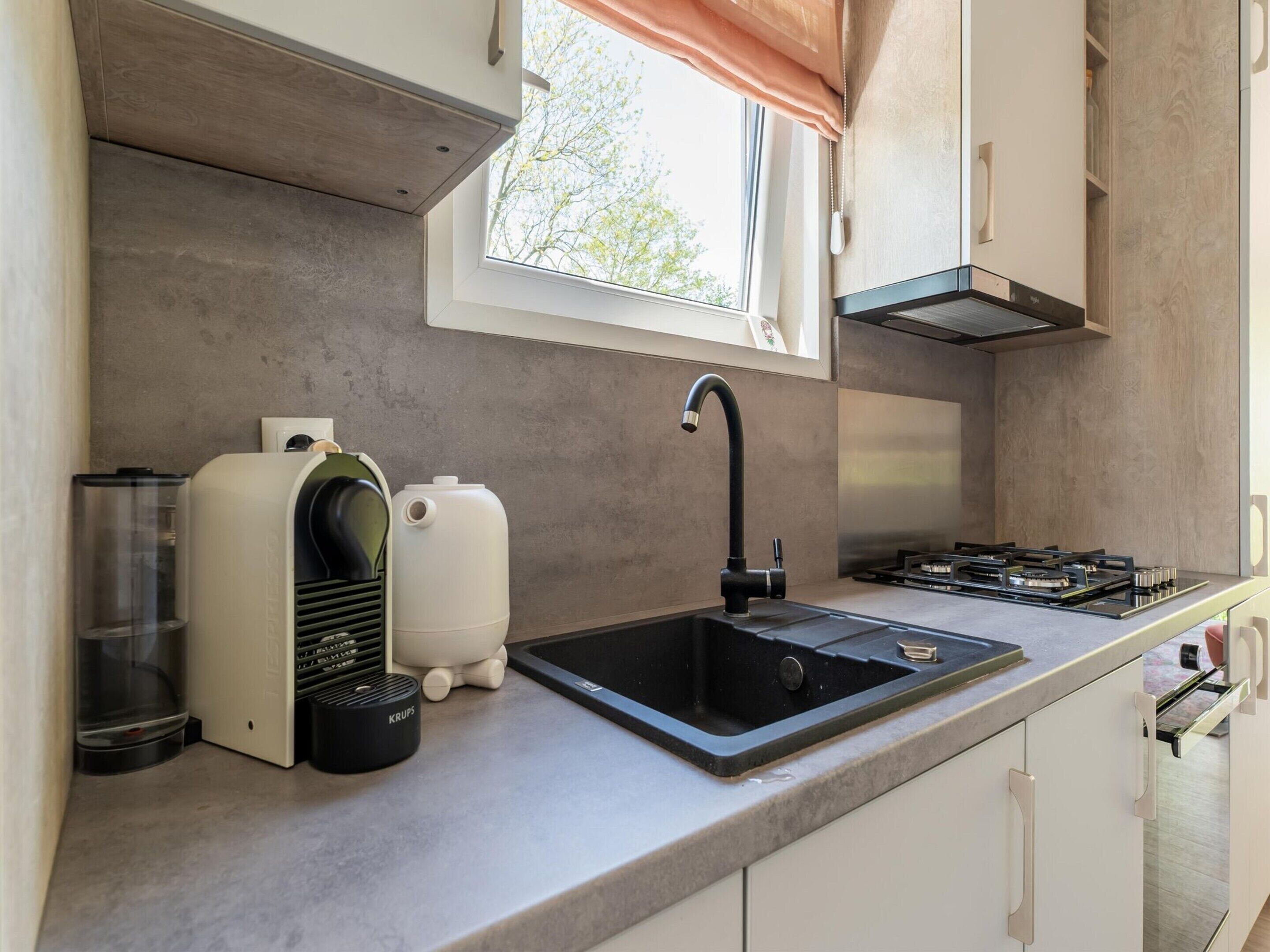 A modern kitchen with a black sink, a built-in stove, and a window with a view of trees.