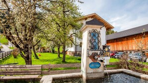 A fountain with a plaque, surrounded by a wooden fence, benches, and a grassy area with trees. - Apartment in Hainzenberg Near Ski Slopes (Hainzenberg)