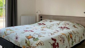 Une chambre à coucher avec une couvre-lit à motifs floraux, un radiateur, une fenêtre avec des rideaux et une lampe de chevet.